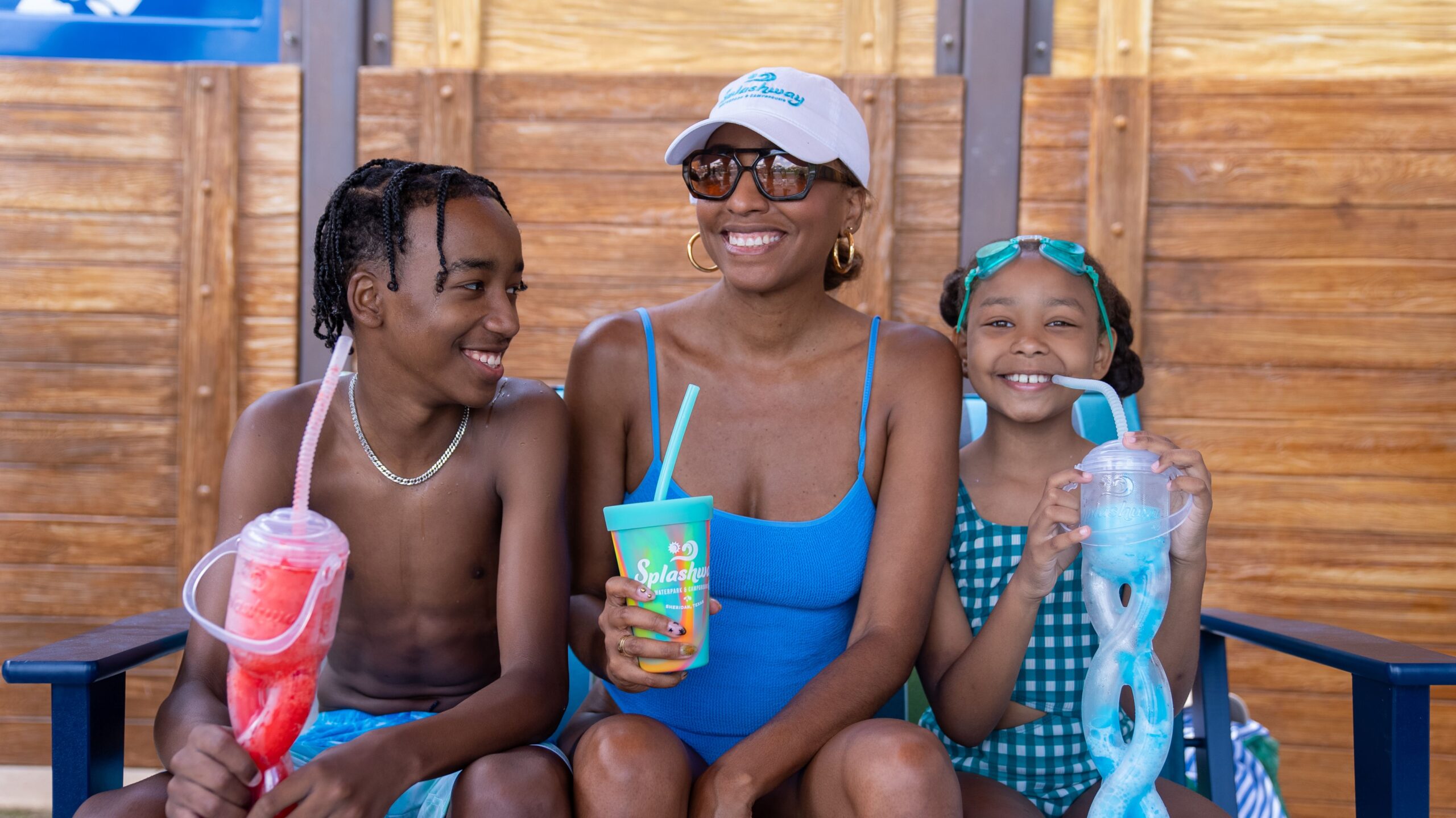 A smiling family in swimwear enjoying colorful drinks at a waterpark seating area.